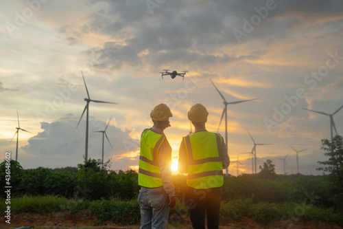 Teamwork of Asian windmill engineer group, worker working, control a drone on site at wind turbines field or farm, clean energy source. Eco technology for electric. industry nature environment. People photo