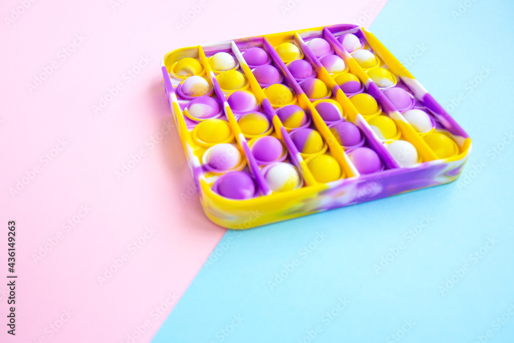 Trend bright multicolored antistress toy Popit. Poppit new fidget toy on empty pink and blue background. Close up Trend bright multicolored antistress toy Popit. Poppit new fidget toy on empty pink and blue background. Close up