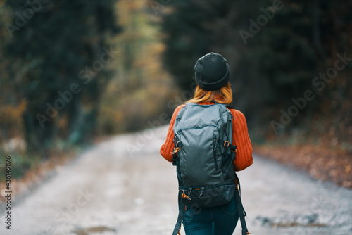 woman with a backpack in a hat and an orange sweater on the road in the autumn forest back view © SHOTPRIME STUDIO