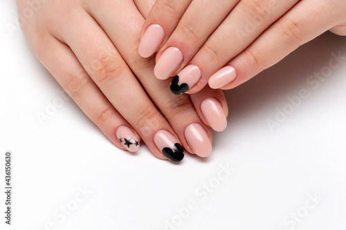 Exclusive manicure. Beige  nude manicure with painted black stars and a silhouette of a mouse on long oval nails close-up on a white background.