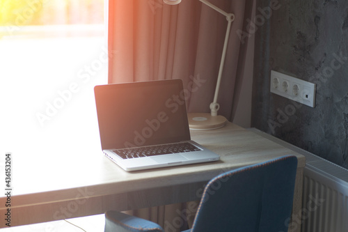 Workplace at home interior. A work desk in front of a sunny window. Interior of a room and a table-sill with a computer and an armchair 