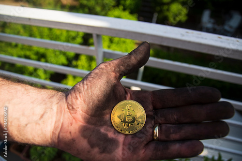 A miner proudly displays his newly mined and holding bitcoin among black coals. Selective Focus Coin.