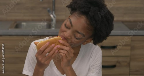 Tilting camera of African woman eating hot dog at home. Fast food. Junk food