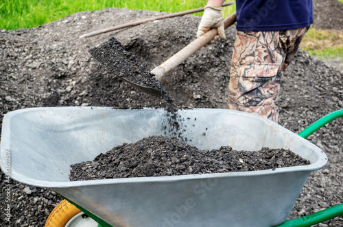 Wallpaper Mural unidentified man pours gravel into a wheelbarrow. as part of a construction project, a man is transporting rubble on a hand wheelbarrow. Paving the road with gravel. Construction with your own hands Torontodigital.ca