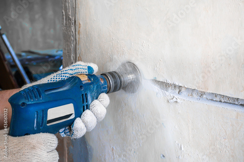 drills a hole for an electrical outlet in a concrete brick wall.  Construction worker man with pneumatic hammer drill hammer drill with diamond crown makes a hole in the wall for electrical cable photo