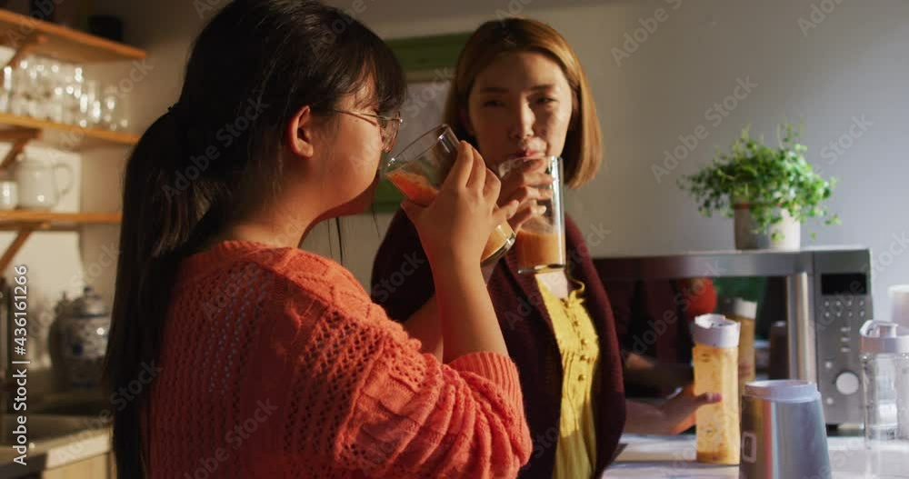 Asian mother and daughter drinking healthy drink in kitchen smiling Asian mother and daughter drinking healthy drink in kitchen smiling