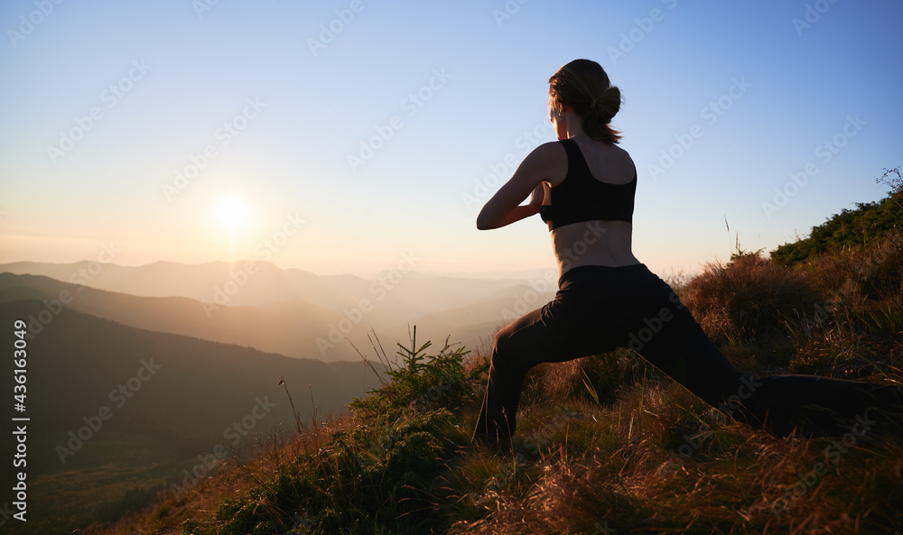 Back view of woman practicing yoga in Warrior pose in the evening. Female is meditating in the mountains and watching sunset. Concept of harmony with nature. Back view of woman practicing yoga in Warrior pose in the evening. Female is meditating in the mountains and watching sunset. Concept of harmony with nature.