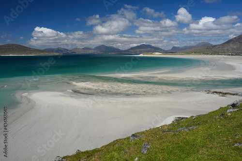 Seilebost and Luskentyre beaches on a bright sunny day. Isle of Harris, Scotland. Taken from high viewpoint. White sand, turquoise and blue sea, mountains, grassy hill foreground.