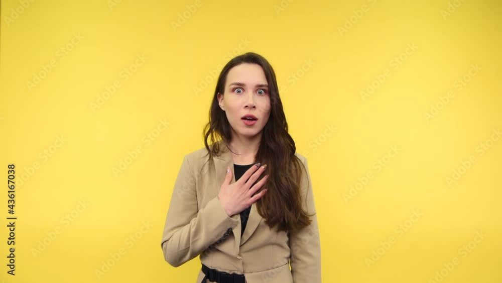Portrait of a shocked lady in a jacket stands on a yellow background and looks at the camera with her hands raised and her mouth open in surprise. Portrait of a shocked lady in a jacket stands on a yellow background and looks at the camera with her hands raised and her mouth open in surprise.