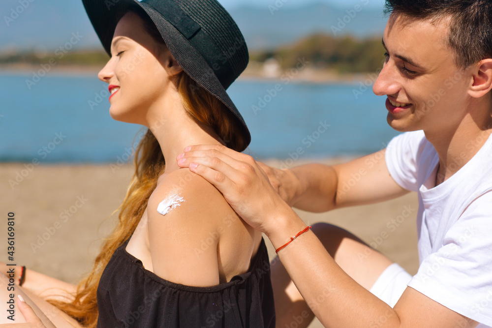 Suncare couple on a summer beach vacation have good skincare with high spf sunblock. Couple applying suncream. Handsome man putting sun tan lotion on his girlfriend at the beach. Vacation, tourism.
