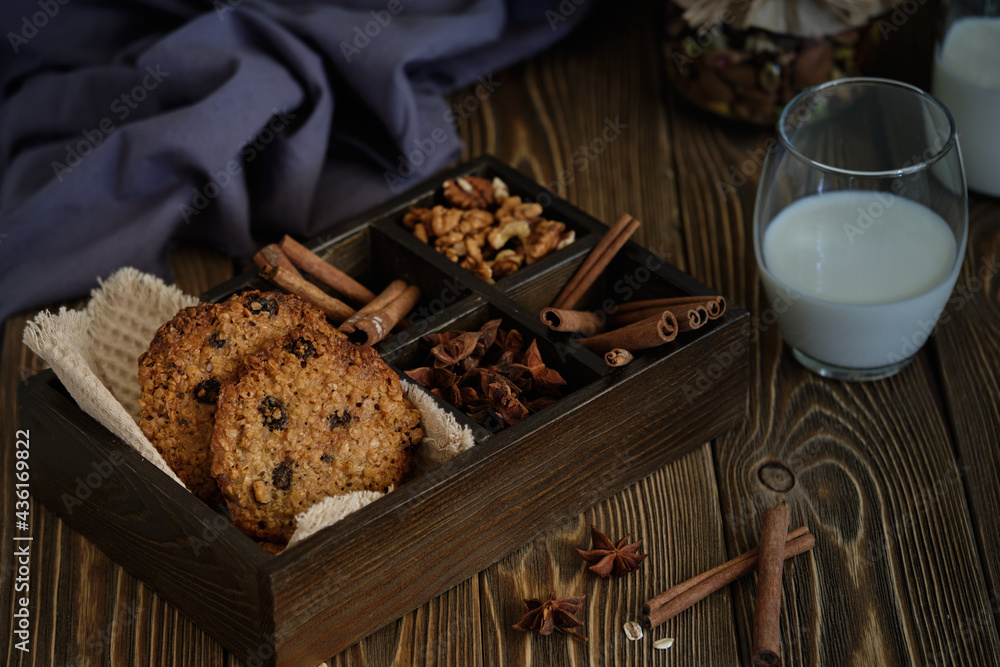 Fototapeta premium Delicious and flavorful oatmeal cookies with nuts, raisins and spices with a cup of milk on old wooden table