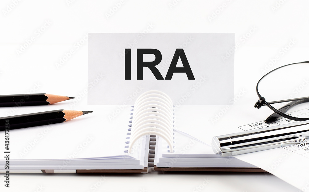 Text IRA on paper card,pen, pencils,glasses,financial documentation on table - business concept Text IRA on paper card,pen, pencils,glasses,financial documentation on table - business concept