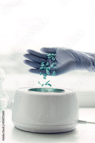 Depilatory master puts wax capsules into the wax melter, close-up