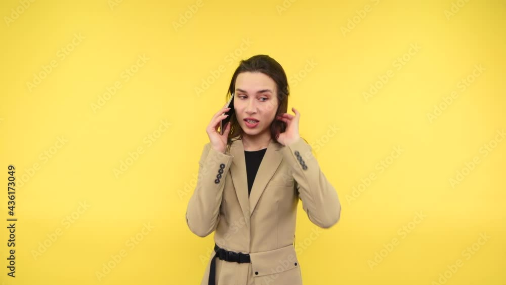 Dissatisfied business woman in a suit communicates on the phone on a yellow background. Dissatisfied business woman in a suit communicates on the phone on a yellow background.