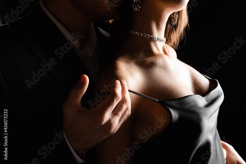 cropped view of sensual woman in silk dress with male hand on shoulder isolated on black photo