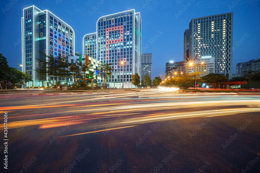 Obraz premium Cityscape of a street in Hanoi with high buildings during sunset time with blurred cars running on street