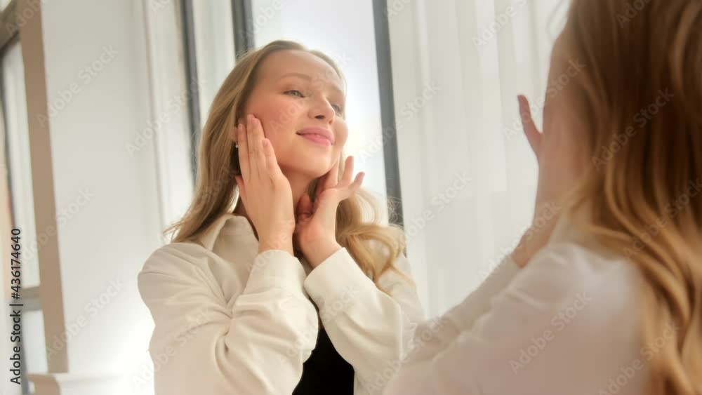 Young blonde woman looking touching face in the mirror examining skin condition and enjoy her healthy skin. Beauty product concept. Young blonde woman looking touching face in the mirror examining skin condition and enjoy her healthy skin. Beauty product concept.