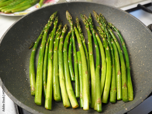 green young thin asparagus fried in a gray round frying pan side view. cooking at home in the kitchen