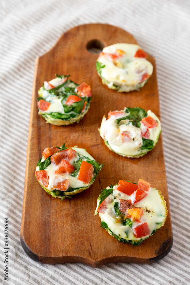 Homemade Egg White Breakfast Cups with Spinach and Tomato on a rustic wooden board, side view.