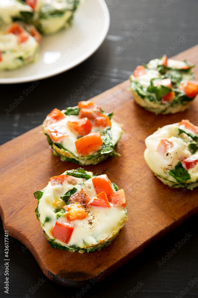 Homemade Egg White Breakfast Cups with Spinach and Tomato on a rustic wooden board on a black background, side view. Homemade Egg White Breakfast Cups with Spinach and Tomato on a rustic wooden board on a black background, side view.