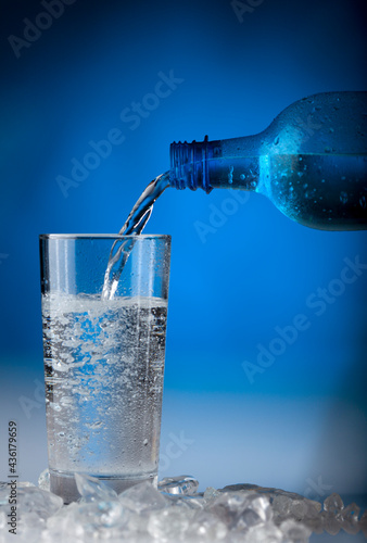 Pouring sparkling table water froma blue bottele into a glass photo