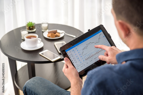 Man trading digital currencies online while relaxing by the cup of coffee in expencive hotel room