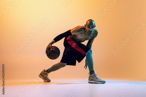 Portrait of african-american professional male basketball player in action in neon light on orange background.