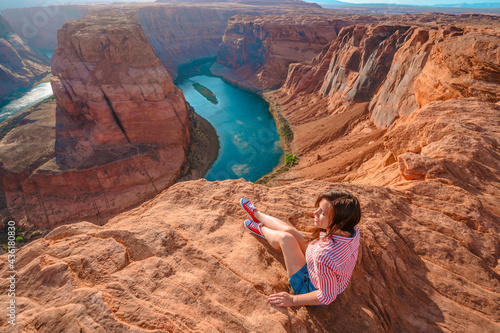 Rear view of a young woman enjoying a view of the incredible Horseshoe Bend, the horseshoe meander of the Colorado River in Page, Arizona.
