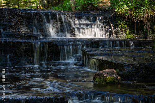 Cascading waterfall cascades in Estonia in green light at summertime