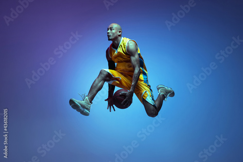 Sportive athletic african-american male basketball player training in neon light on blue background. © master1305