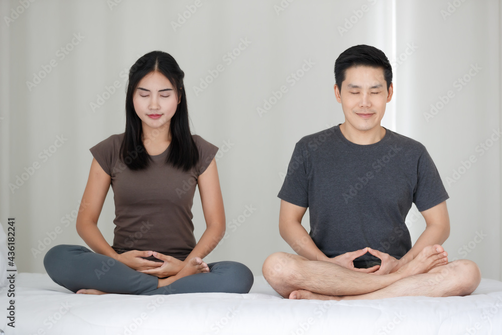 Man and woman Buddhist sitting on bed in the bedroom and doing meditation in Buddhism religion style together. The idea for faith and trust in religion and calm of mind