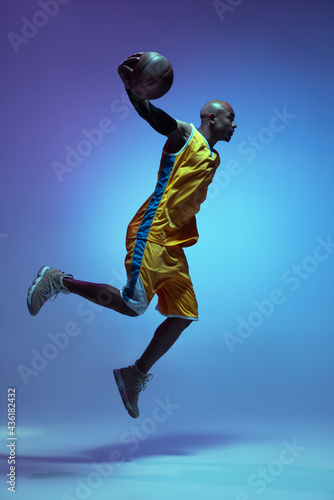 Handsome african-american male basketball player in action and motion in neon light on blue background. Concept of healthy lifestyle, professional sport.
