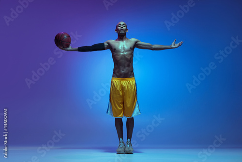 Sportive athletic african-american male basketball player posing in neon light on blue background.