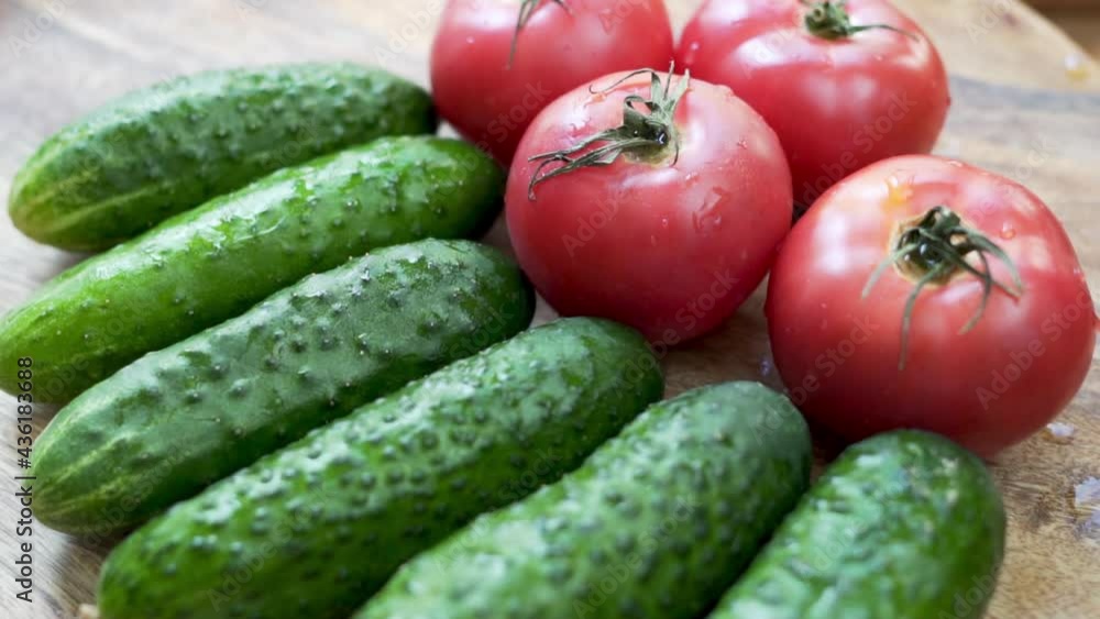 Fresh Cucumbers and Pink Tomatoes on a Wooden Surface, Macro, Isolated Rotation. Background of Ripe Green Cucumbers and Tomatoes, Herbs, Vegetables. Healthy Vegan Food and Diet. 
