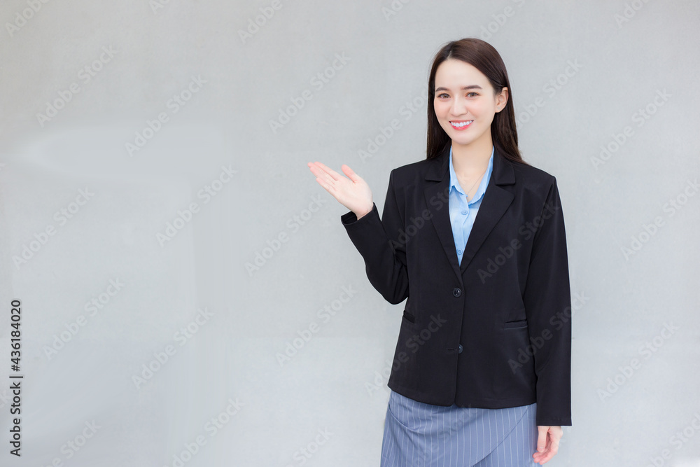 Asian business female who wear black formal suit smiles and shows her hand up to present something on wall. Asian business female who wear black formal suit smiles and shows her hand up to present something on wall.