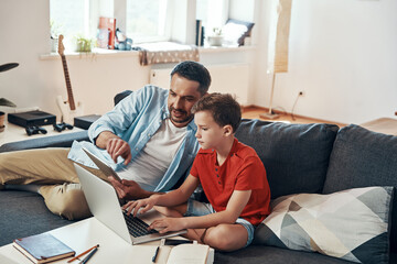 Happy father helping his son with homework while homeschooling in the living room