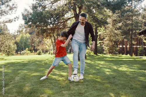 Happy father and son playing football and smiling while having fun on the lawn