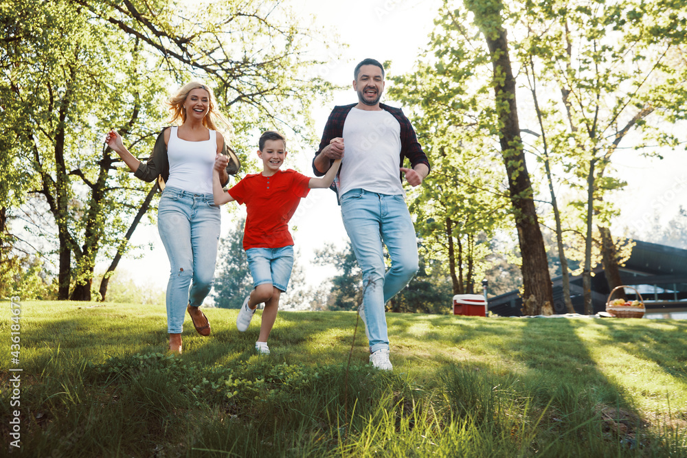 Happy young mother and father with little boy holding hands and walking outdoors