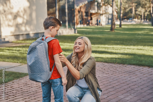 Happy young woman adjusting backpack while preparing her son to school