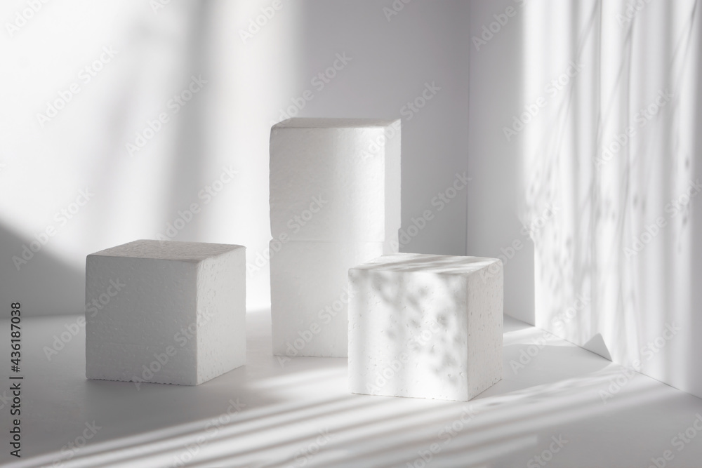 White square stands, different heights, against background of the walls, in rays of sunlight. Concept of presentation of products, packaging, cosmetics. 3d podium for various products White square stands, different heights, against background of the walls, in rays of sunlight. Concept of presentation of products, packaging, cosmetics. 3d podium for various products