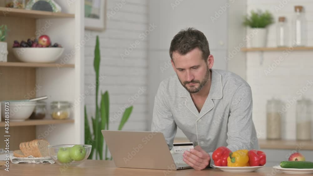 Man making Online Payment on Laptop in Kitchen Man making Online Payment on Laptop in Kitchen