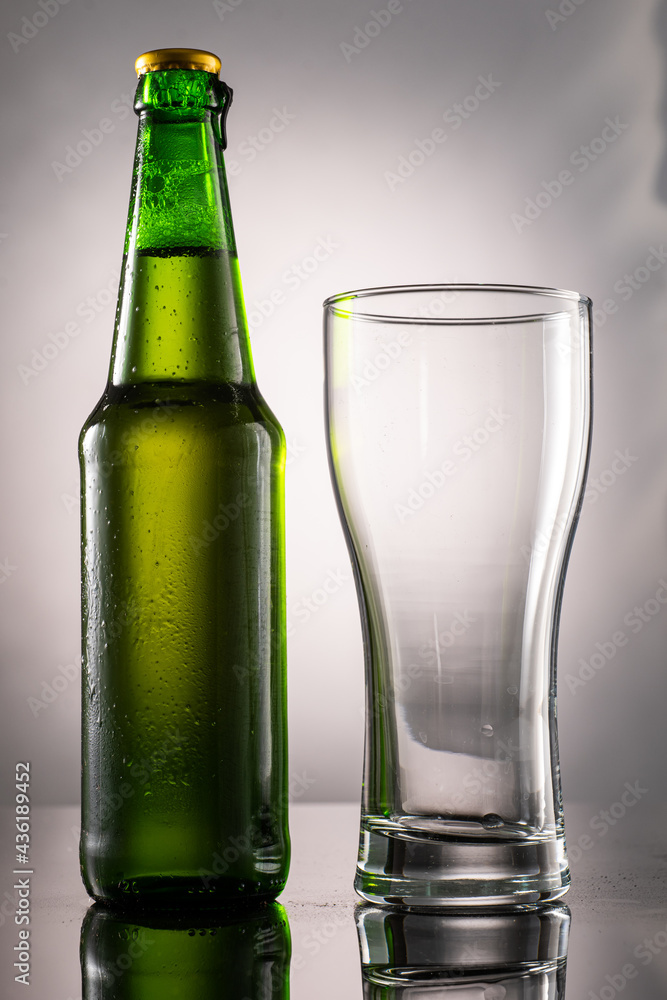 pouring beer into beer glass and foam and green transparent bottle with beer beside pouring beer into beer glass and foam and green transparent bottle with beer beside