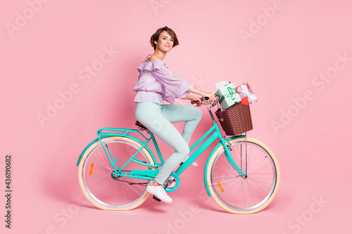 Photo of charming lady ride bicycle basket gifts wear violet blouse trousers shoes isolated pink color background © deagreez