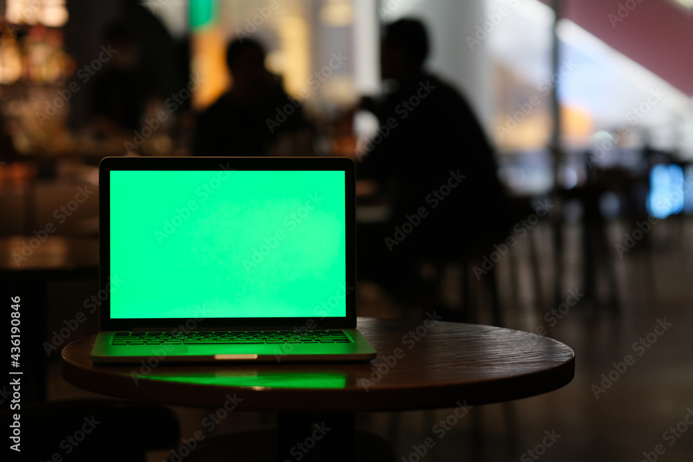 green screen laptop computer on bar table at night. Blur people communicate in dark
