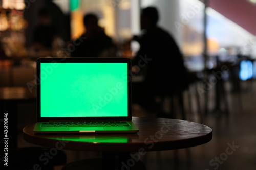 green screen laptop computer on bar table at night. Blur people communicate in dark