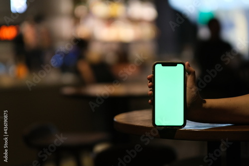 Wallpaper Mural close up hand showing green screen phone on bar table at night. colorful bokeh Torontodigital.ca
