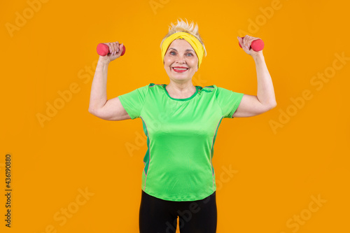 old beautiful woman with dumbbells on yellow background  © Alexandr