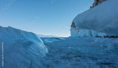 On the frozen lake there are blue shiny ice hummocks. Icicles on a frozen rock base. Clear sky. Winter day. Baikal