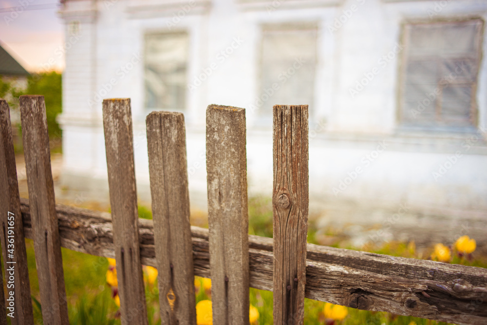 Old broken picket fence. White rural house in blurred background