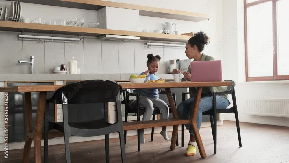 A little african girl feeding her mom from the hands while sitting in the kitchen A little african girl feeding her mom from the hands while sitting in the kitchen